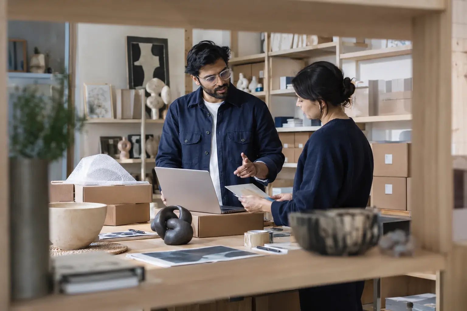 Un entrepreneur comparant les options de livraison avec un collègue. Produits : estampes et objets de design.