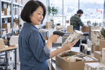 Membre de l’équipe de traitement des commandes vérifiant un produit avec un lecteur de codes-barres portatif à une table d’emballage