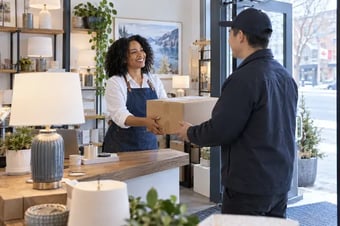 Responsable des expéditions d’une petite entreprise remettant un colis emballé à un coursier à l’entrée lumineuse d’une boutique