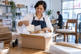 Merchant arranging matching tissue paper, a simple thank-you card and protective packaging for a customer order