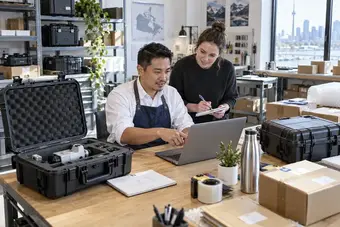 Spécialiste en développement logiciel et responsable du traitement des commandes discutant d’une intégration d’expédition devant un ordinateur portable, dans un bureau de logistique