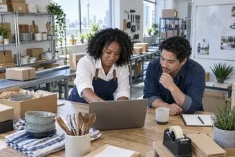 Software developer and fulfilment lead discussing a shipping integration at a laptop in a logistics office